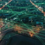 Vue aérienne d'une ville au crépuscule avec un réseau lumineux de fibres optiques superposé, symbolisant la culture numérique et l'interconnexion moderne.