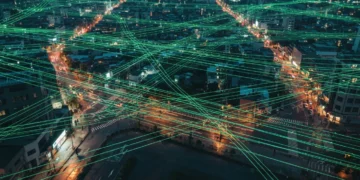 Vue aérienne d'une ville au crépuscule avec un réseau lumineux de fibres optiques superposé, symbolisant la culture numérique et l'interconnexion moderne.