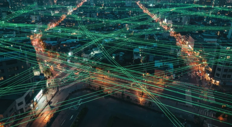 Vue aérienne d'une ville au crépuscule avec un réseau lumineux de fibres optiques superposé, symbolisant la culture numérique et l'interconnexion moderne.