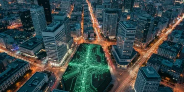 Vue aérienne urbaine au crépuscule, des lumières vertes symbolisent les flux de connexion numérique et les habitudes modernes redéfinies par la technologie.