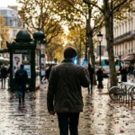 Une personne, vue de dos, marchant dans une rue parisienne animée, son visage éclairé par l'éclat subtil d'un smartphone, soulignant la digitalisation omniprésente et l'isolement dans la foule.